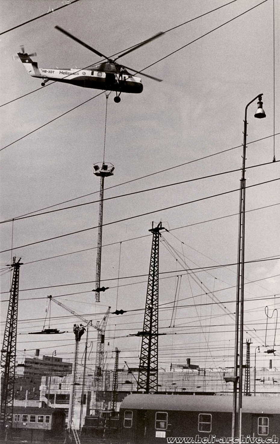 15 giugno 1974 - L'S-58T impegnato nella posa di nuovi lampioni presso la stazione ferroviaria di Francoforte. L'uomo appeso a lato della cabina fornisce al pilota Walter Tschumi le necessarie indicazioni (HAB)
