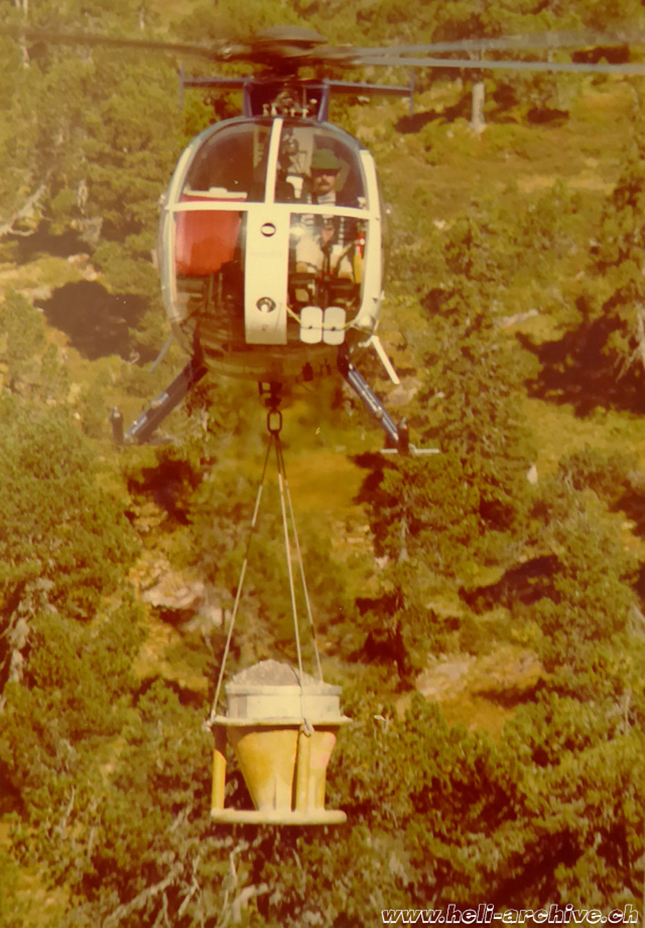 1977 - Peter Kolesnik at the controls of the Hughes 500D HB-XFR loaned by Fuchs Helikopter trasports gravel for a mountain construction site (family Kolesnik)