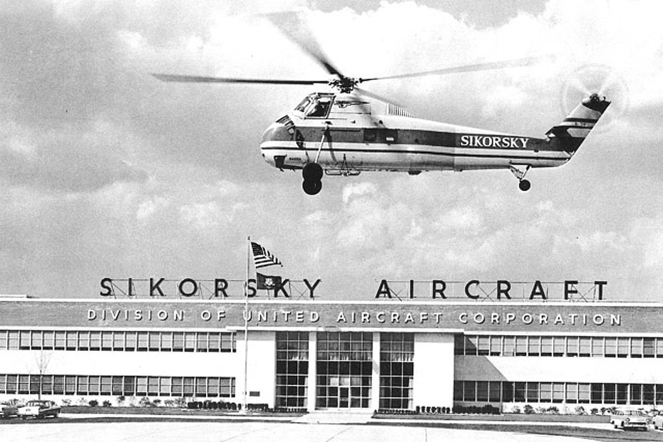 The Sikorsky S-58B N408A in flight in front of the Sikorsky fabric in Stratford (HAB)